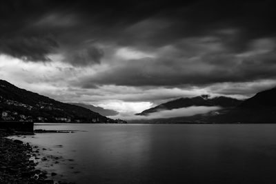 Scenic view of sea and mountains against storm clouds