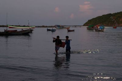 Rear view of men standing on boat in sea against sky