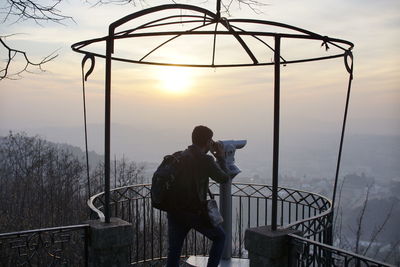 Man photographing on railing against sky