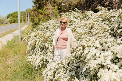 Elderly woman posing among bushes with white flowers