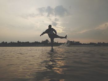 Silhouette man jumping in sea against sky during sunset
