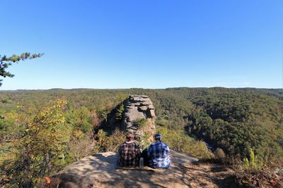 People sitting on mountain against clear sky