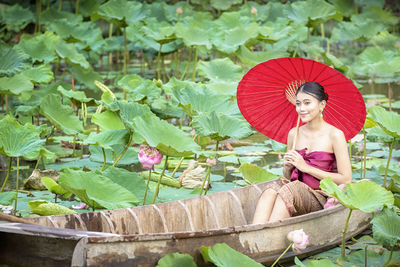 Smiling young woman holding umbrella while sitting on boat