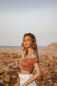 Portrait of beautiful woman standing on beach against sky