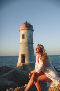 Side view of woman sitting on rock against clear sky