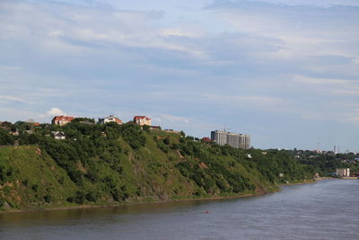 Trees and buildings by sea against sky