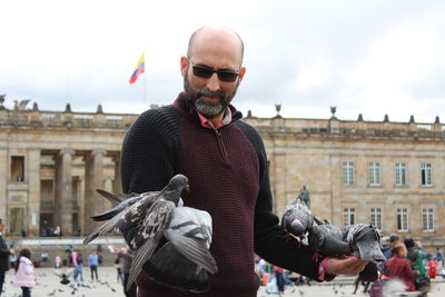 Man feeding pigeons on hands at town square in city against sky