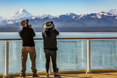 Rear view of man and woman photographing snowcapped mountain