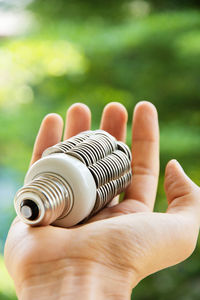 Cropped hand of man holding light bulb against plants