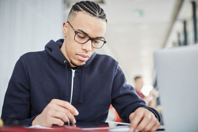 Serious male university student using digital tablet while sitting at table in cafeteria