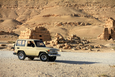 A rugged off-road vehicle travels through an expansive desert with majestic mountains and a blue sky