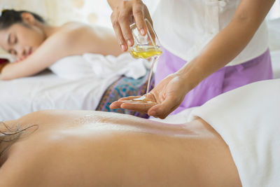 Massage therapist putting oil on back of woman in spa