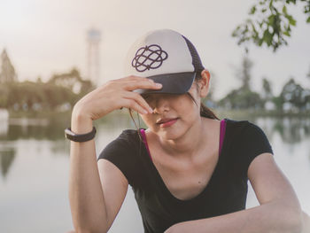 Portrait of young woman holding hat against water