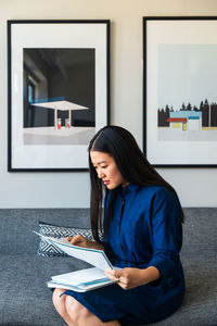 Young businesswoman reading documents while sitting on sofa at office