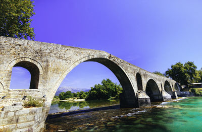 Low angle view of arch bridge over river against clear blue sky