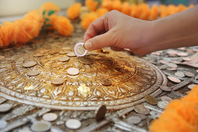 Close-up of hand putting coin into religious coin bank