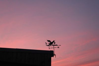 Low angle view of silhouette weather vane against orange sky