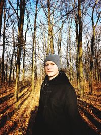 Portrait of young man standing against bare trees in forest