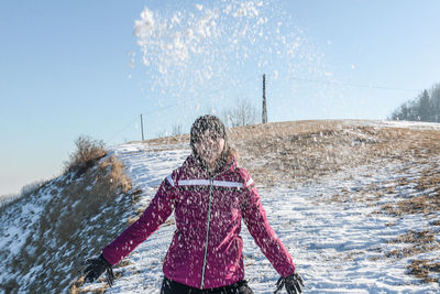 Woman playing with snow while standing against clear sky
