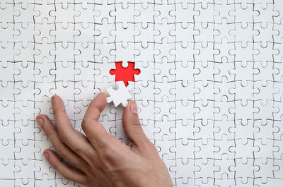 Cropped hand holding jigsaw piece over puzzle