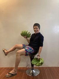 Portrait of smiling young woman sitting on table against wall at home