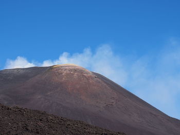 Low angle view of volcanic mountain against blue sky