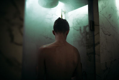 Rear view of shirtless man standing against wall at home