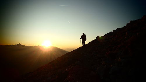 Silhouette man standing on rock against sky during sunset