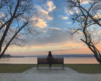 Rear view of man sitting on bench at sunset