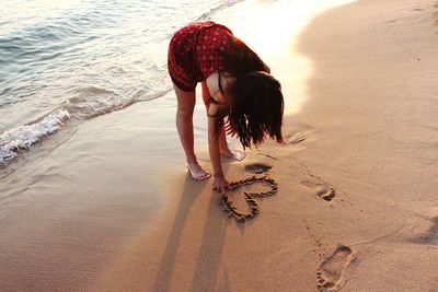 High angle view of woman making heart shape on shore at beach