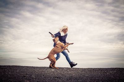 Woman with dog at field against cloudy sky