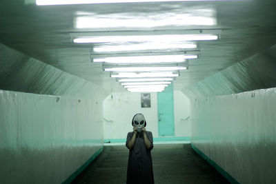 Woman covering face with mask in illuminated corridor