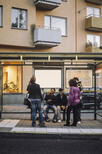 Happy male and female friends having fun at bus stop in city