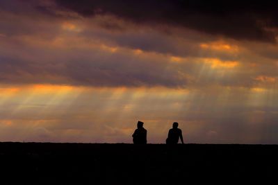 Silhouette men standing on land against sky during sunset