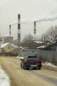 Car on snow covered factory against sky during winter