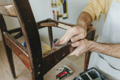 Hand of man polishing chair using sand paper at home