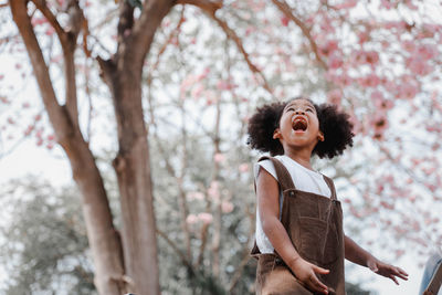 Young woman looking up while standing against tree