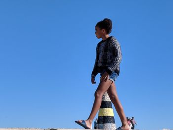 Low angle view of girl standing against blue sky