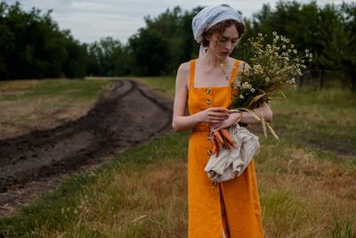 Woman holding a flower and carrots standing in a field 