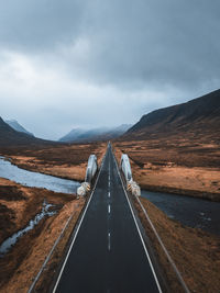 Empty road leading towards mountains against sky