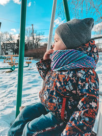 Boy sitting on swing during winter