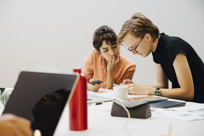 Colleagues sharing smart phones while sitting in illuminated board room during meeting