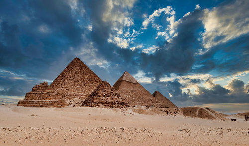 View of desert against cloudy sky with pyramid