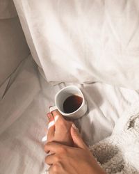 Midsection of person holding coffee cup on bed