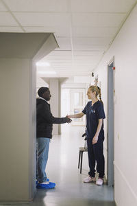 Female nurse doing handshake with male patient while standing in hospital corridor