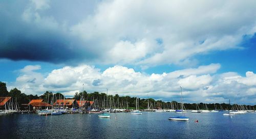 Boats moored in calm sea against cloudy sky