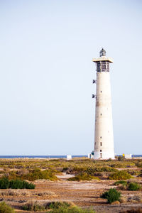 Lighthouse by road against clear sky
