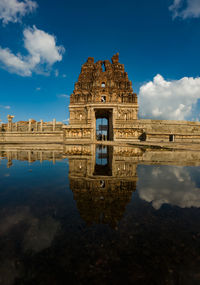 Reflection of temple by water in city against sky