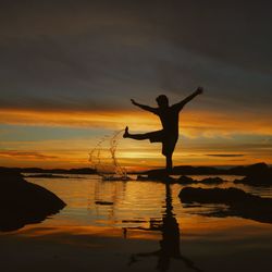 Silhouette person standing by sea against sky during sunset