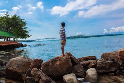 Rear view of man standing on rock by sea against sky